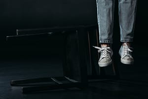 cropped view of self-murder legs hanging near fallen chair on black background