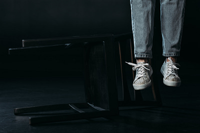 cropped view of self-murder legs hanging near fallen chair on black background